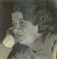 A black and white photo. A woman with short brown hair rests her face on her hands.
